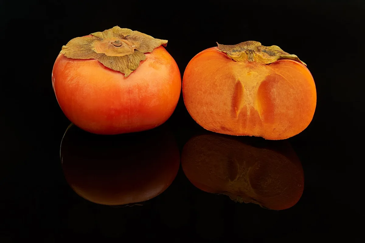 Twee oranje persimmon-kaki's, één heel en één doorgesneden met zichtbaar oranje vruchtvlees.