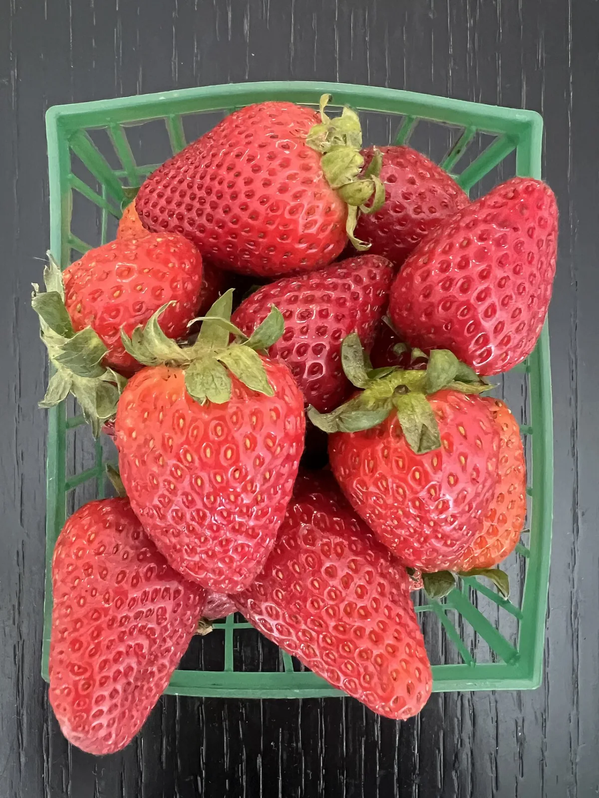 Verse aardbeien met kroontje in een groen fruitbakje.